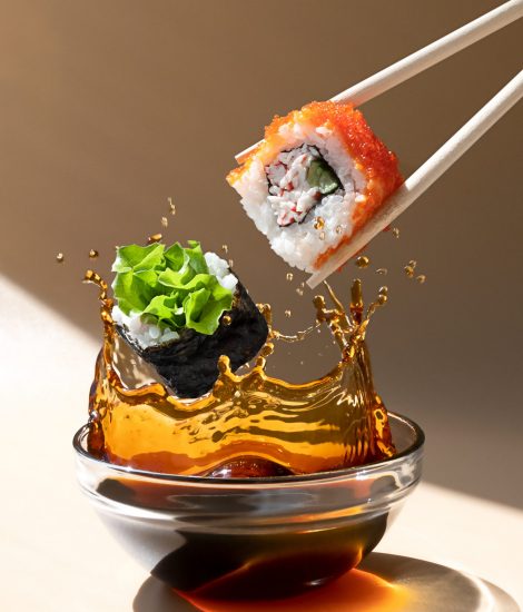 Fresh sushi roll falling into a dish of soy sauce with a splash of liquid in a freeze motion.